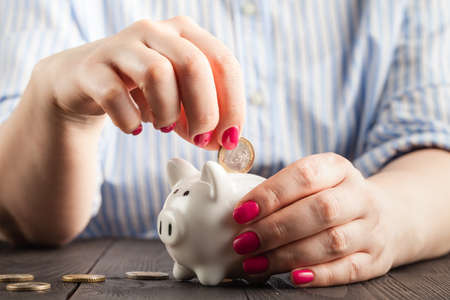 savings concept,white piggy bank with human female hand inserting  coin insideの写真素材