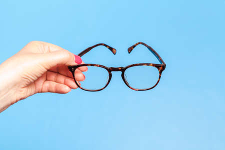 Woman hand holding spectacles on blue backgroundの写真素材