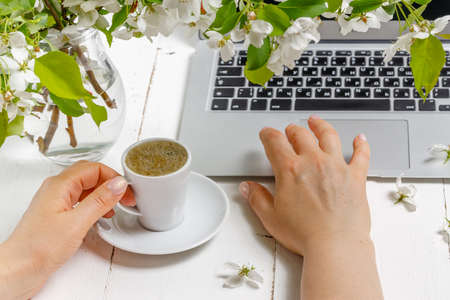 Modern feminine workplace concept. Laptop, coffee, beautiful apple tree flowers  on the white table, top viewの写真素材