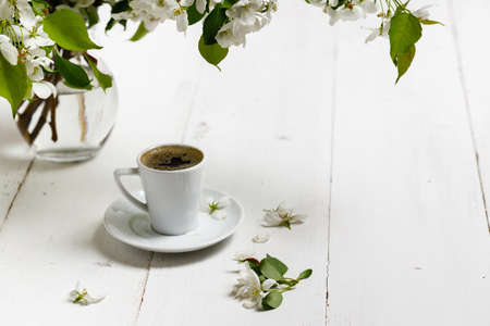 Spring still life. Cup of coffee with apple tree flowers and petals of flowers are on white cafe table outside in blooming gardenの写真素材