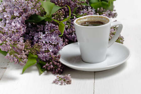 Little delicate elegant bouquet of spring flowers and a teacup on white wooden table, morning breakfastの写真素材