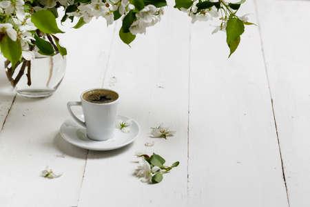 Spring still life. Cup of coffee with apple tree flowers and petals of flowers are on white cafe table outside in blooming gardenの写真素材