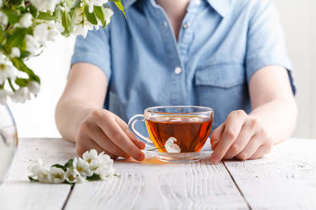 Girl having a cup of tea on table covered with apple tree flowersの写真素材