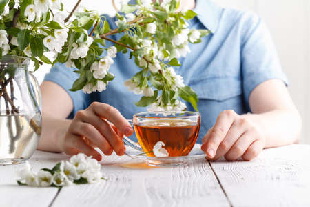 spring morning, the girl drinks tea with a bouquet of spring apple flowers in a vase. The concept of youth and femininityの写真素材