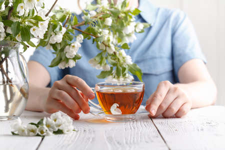 Girl having a cup of tea on table covered with apple tree flowersの写真素材