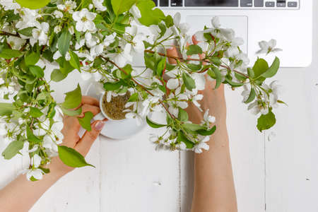 Work space with a laptop, a cup of tea and flowers on the wooden background. Home office composition, freelance conceptの写真素材