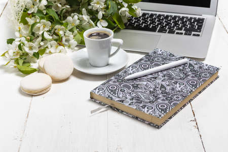 Feminine business concept with laptop, spring flowers bouquet and woman's hands holding cup of warm tea or coffeeの写真素材