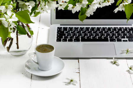 Workspace with girl's hand on laptop keyboard and cup of coffee, white spring apple tree flowers on white woodden background. View feminine office table desk. Freelancer working placeの写真素材