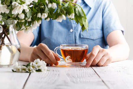 Girl having a cup of tea on table covered with apple tree flowersの写真素材
