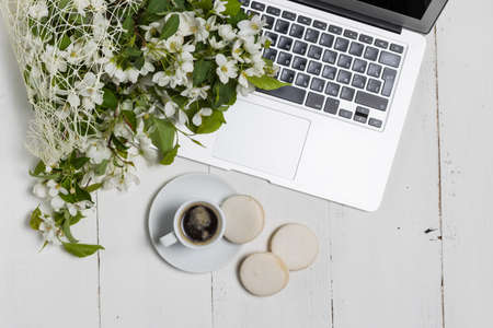 Feminine business concept with laptop, spring flowers bouquet and woman's hands holding cup of warm tea or coffeeの写真素材