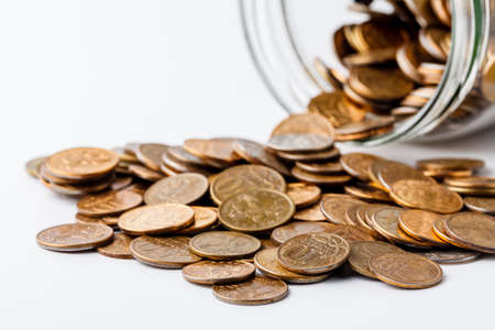 Coins placed on glass jar and coins scattered around the glass jarの写真素材