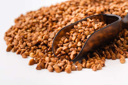 Food ingredients: heap of buckwheat in a wooden scoop, on white background の写真素材