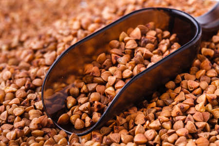 raw buckwheat groats in a wood plate on a buckwheat backgroundの写真素材