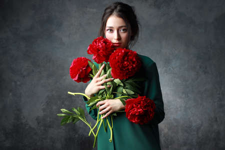 Beautiful girl in tender green dress with bouquet flowers peonies in hands. Playful fashion model looking at cameraの写真素材