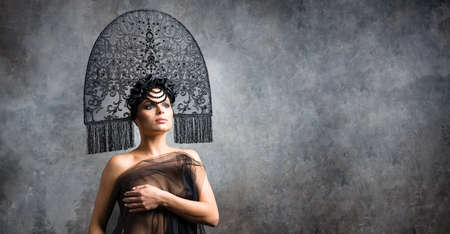 Young sexy woman brunette in stylish neofolk black kokoshnik stands on stone backgrountの写真素材