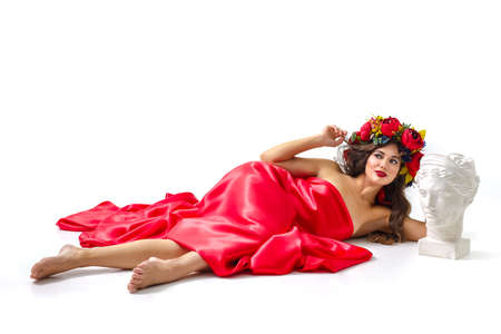 Beautiful woman with flowers in her red hair she is lying relaxed on whiteの写真素材