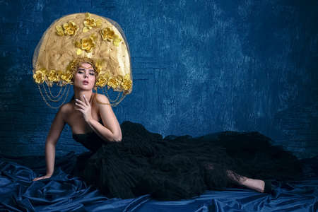 Perfect Woman in dlack Dress and gold hat. Beautiful Fashion Model on Blue Backgroundの写真素材