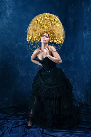 Perfect Woman in dlack Dress and gold hat. Beautiful Fashion Model on Blue Backgroundの写真素材