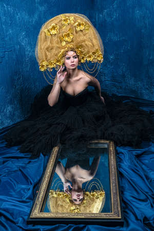 Perfect Woman in dlack Dress and gold hat. Beautiful Fashion Model on Blue Backgroundの写真素材