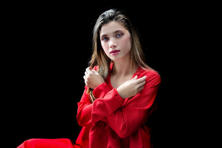 Gorgeous young woman in red dress posing against dark studio backgroundの写真素材