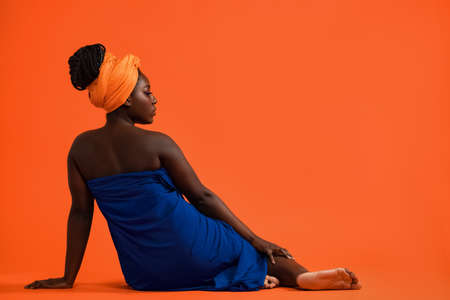 Cheerful young African woman in a simple blue dress on orange backgroundの写真素材