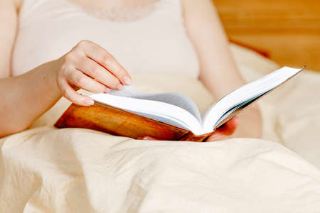 Girl holding wineglass with white wine and old book. Woman reading book and drinking wine at home, self-isolationの写真素材