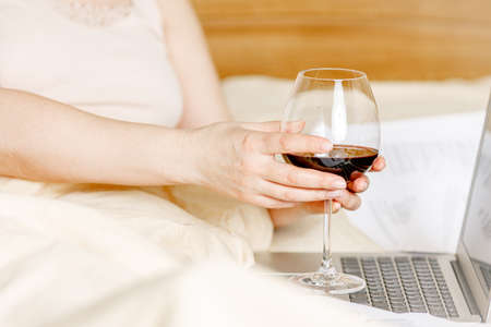 Woman lying on bed & watching computer tablet and drinking a glass of wine, no bra, stay homeの写真素材