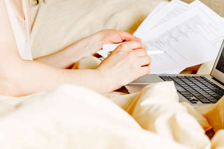 Working woman freelancer in casual clothes with laptop and cup wake up in the bed at home in bright...