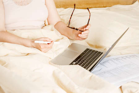 woman working on a laptop laying on the bed in the house. Freelancer woman working on her laptop at home with glass of wineの写真素材
