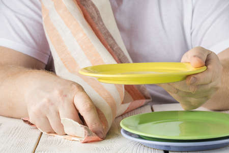 Close up mans hand wipe with towel a clean plate after washing all the dishes with dishwasher liquid in the vintage kitchen with wood cupboard and stone water tap and washstandの写真素材