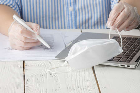 Coronavirus. Woman cleaning her hands at the office. Sick with mask for corona virus. Workplace desk with computer. Woman spraying alcohol gel or antibacterial soap sanitizerの写真素材