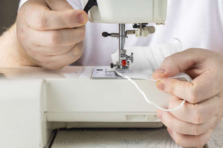 disposable face shield and homemade multi-face mask lie on the sewing machine, blue background, make...