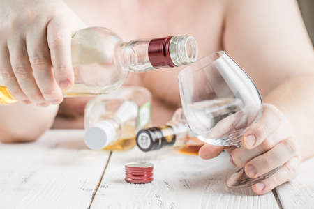 Alcohol addicted man at the table. Sad depressed male adult having troubles with alcohol.の写真素材