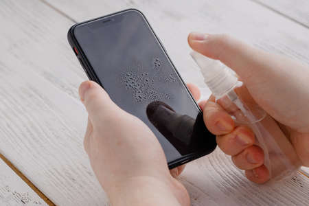 Covid 19 prevention applying alkohol desinfection to mobile phoneの写真素材