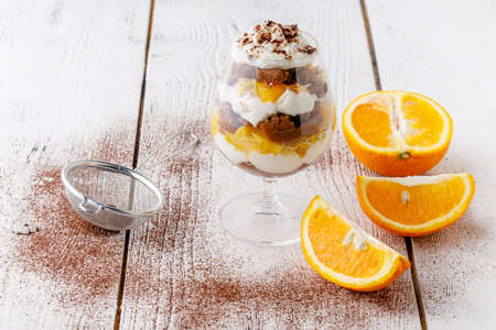 creamy trifle in beautiful glasses and cut fresh ripe fruit on white wooden background - healthy...