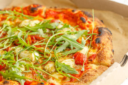 Close up of pizzas with variety of toppings and cheese in cardboard take out boxes with open lid on wooden tableの写真素材