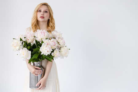 Indoor shot of beautiful girl holding white and rose peonies, winsome woman with big bouquet, enjoying her flowersの写真素材