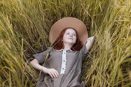 red-haired girl lies in the grass on a summer meadow at sunset in an elegant dressの写真素材