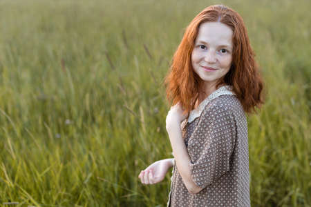 redhead girl posing on a summer meadow at sunset in an elegant dressの写真素材