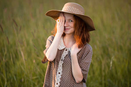 redhead girl posing on a summer meadow at sunset in an elegant dressの写真素材
