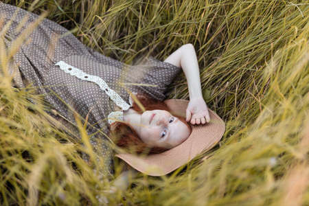 red-haired girl lies in the grass on a summer meadow at sunset in an elegant dressの写真素材