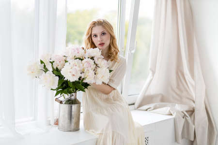 Indoor shot of beautiful girl holding white and rose peonies, winsome woman with big bouquet, enjoying her flowersの写真素材
