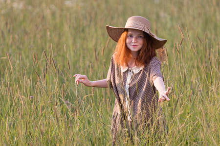 redhead girl posing on a summer meadow at sunset in an elegant dressの写真素材