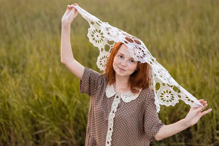 redhead girl posing on a summer meadow at sunset in an elegant dressの写真素材