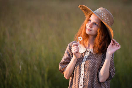 emotional redhead girl playing in the grass on a summer meadow at sunset in an elegant dressの写真素材