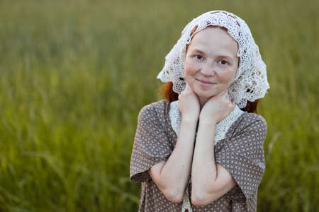 emotional redhead girl playing in the grass on a summer meadow at sunset in an elegant dressの写真素材
