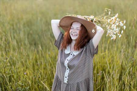 redhead girl posing on a summer meadow at sunset in an elegant dressの写真素材