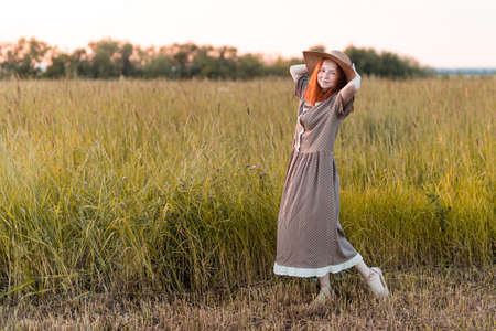 emotional redhead girl playing in the grass on a summer meadow at sunset in an elegant dressの写真素材
