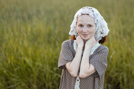 emotional redhead girl playing in the grass on a summer meadow at sunset in an elegant dressの写真素材