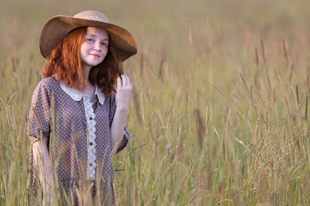 redhead girl posing on a summer meadow at sunset in an elegant dressの写真素材